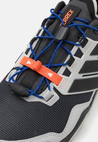 Svarte sportsko laget av mesh og syntetiske materialer. Har elastiske snørebånd med en oransje lås, grå detaljer og en teksturert såle.