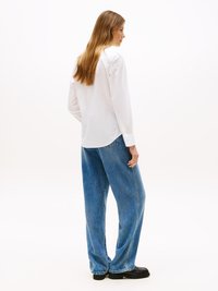Chemise blanche à manches longues avec boutons, associée à un jean bleu en denim oversize et des chaussures noires. Tissu doux avec une coupe décontractée.