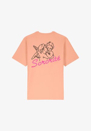 Gaišs persiku krāsas t-krekls, kurā redzams melns kontūrzīmējums ar diviem eņģelīšiem, kas apskauj viens otru, un zem tā burtiski rozā slīpā fontā rakstīts "Sororité".