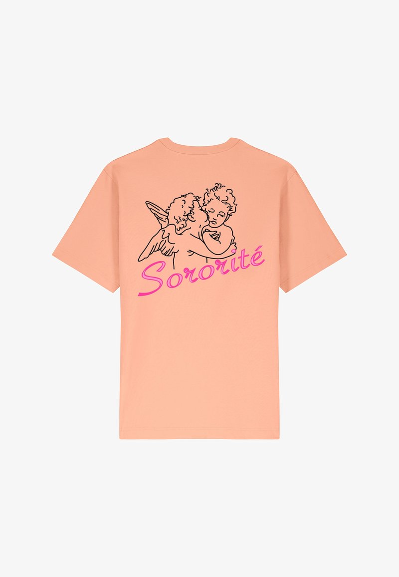 Gaišs persiku krāsas t-krekls, kurā redzams melns kontūrzīmējums ar diviem eņģelīšiem, kas apskauj viens otru, un zem tā burtiski rozā slīpā fontā rakstīts "Sororité".