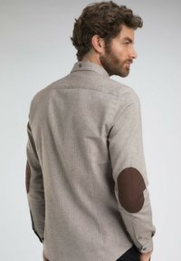 Chemise à motifs marron et gris avec un col boutonné, dotée de coudières marron et de manches longues. Texture de tissu lisse.