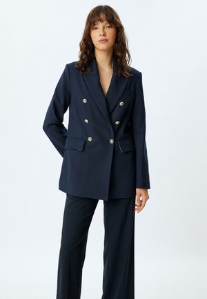 Blazer croisé bleu marine avec boutons dorés, design à rayures, revers crantés et poches avant ; associé à un pantalon assorti.