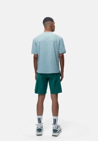 Šviesiai mėlyna trumpa rankovė marškinėliai su apvaliu kaklu, derinami su žaliais kargo šortais, turinčiais šonines kišenes ir baltais dryžuotais kojinėmis.