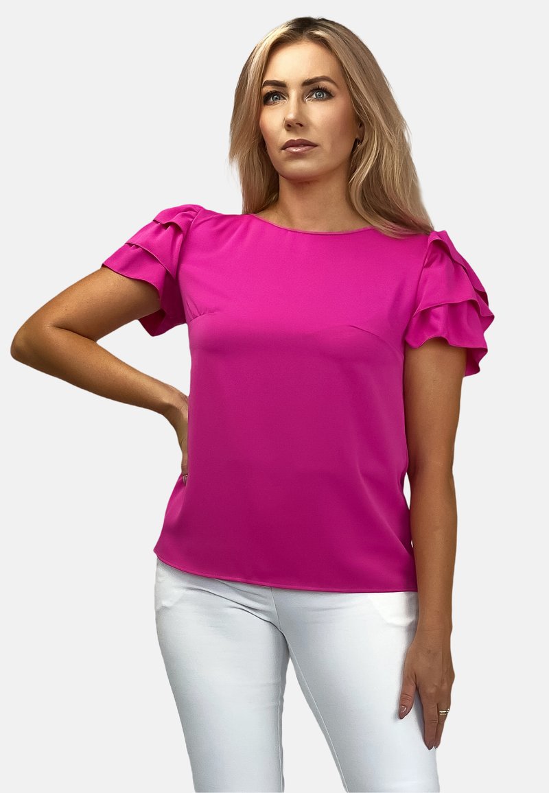 Fuksjowa bluzka z krótkimi, falbaniastymi rękawami, wykonana z gładkiego materiału. Połączona z białymi spodniami, z okrągłym dekoltem i luźnym krojem.