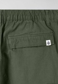 Pantaloni verdi con una cintura elastica, una tasca sul retro e un piccolo etichetta del marchio. Il tessuto presenta una texture liscia e leggera.