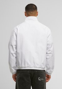 White lightweight jacket with a high collar, elastic cuffs, and hem. Smooth texture, simple design with minimalistic details and no visible logos.