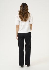 Weiße strukturierte Bluse mit Puffärmeln, kombiniert mit hoch taillierten schwarzen Hosen. Das Outfit hat einen lässigen Schnitt und schmale Beine.