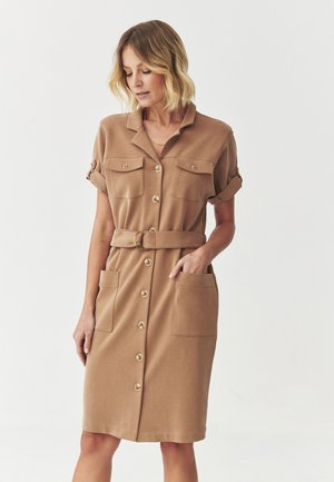 Hellbraunes Hemdblusenkleid mit Kragen, hochgekrempelten Ärmeln, zwei Brusttaschen und einem Taillengürtel, aus glattem Stoff und mit goldenen Knöpfen.