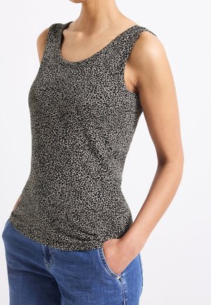 Ärmelloses schwarzes und beiges Top mit Animal-Print, getragen mit blauen Jeans, die Hände lässig in den Taschen, am Hals und an den Hüften gekürzt.