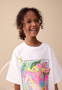 Wit katoenen T-shirt met grote, kleurrijke eenhoorn- en bloemenprint; heeft een ronde halslijn en korte mouwen.