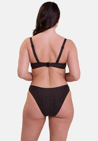 Femme aux longs cheveux noirs portant un bikini scintillant marron foncé vue de dos sur un fond uni.