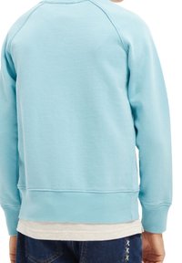 Sudadera azul claro con cuello redondo, puños acanalados y cinturilla. Textura de tela suave, con mangas raglán y sin logotipos visibles.