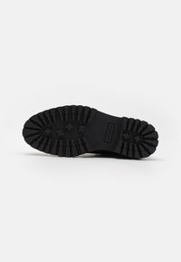 Suela de bota de goma negra con un diseño de profundidad para una mejor tracción, forma redondeada y marca en relieve con una superficie texturizada.