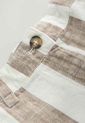 Lähikuva beige-valkoiset raidallisesta kankaasta, johon on ommeltu ruskea nappi vyötärökaitaleen nappiaukon lähelle.