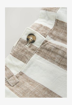 Lähikuva beige-valkoiset raidallisesta kankaasta, johon on ommeltu ruskea nappi vyötärökaitaleen nappiaukon lähelle.