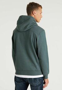 Felpa con cappuccio in tessuto verde tenue, caratterizzata da una vestibilità relaxed, polsini a costine e una tasca a marsupio. Texture liscia con dettagli minimi.