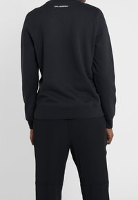 Sudadera negra de manga larga hecha de un tejido suave. Cuenta con un cuello redondo y puños acanalados. Logo mostrado en la parte posterior.