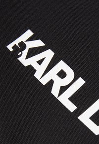 Svart stoff med fet, hvit tekst som leser "KARL" med en logodetalj. Overflaten har en jevn tekstur med et konsistent vevmønster.