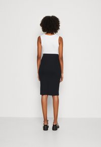 Top bianco senza maniche abbinato a una gonna a tubino nera, aderente e lunga fino al ginocchio. Tessuto liscio con un colore uniforme, design minimalista.