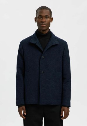 Cappotto in misto lana di colore navy con chiusura a bottoni, colletto a punta e due tasche frontali. Tessuto testurizzato con un motivo sottile.