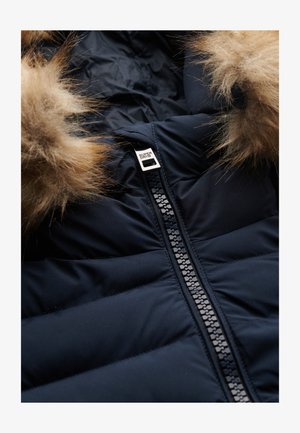 Marineblauwe gewatteerde jas met een afneembare beige bontkap, voorzien van een opvallende zwarte ritssluiting en een zilveren logo-label nabij de kraag.