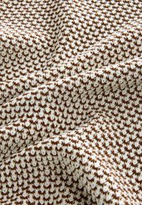 Textured fabric with a white and brown pattern, featuring a knitted design and soft, cozy appearance, suitable for clothing or home decor.