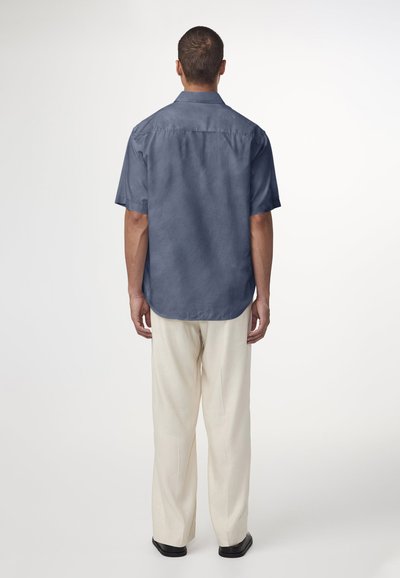 Chemise à col à manches courtes marine, en tissu léger avec une texture lisse, associée à un pantalon ample de couleur claire.