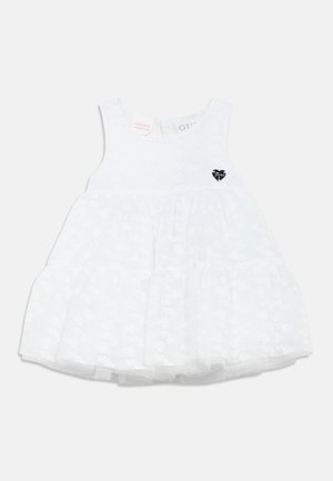 Robe blanche sans manches, ornée d'un motif cœur texturé avec un accent cœur noir. Des couches de tulle forment une jupe évasée.