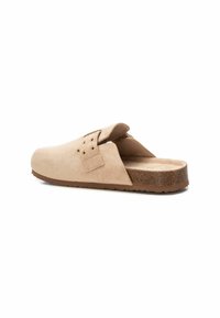 Zoccoli slip-on in suede beige con punta arrotondata, apertura sul retro e suola marrone texturizzata con piccoli fori di ventilazione e hardware semplice.