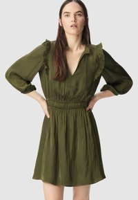 Zielona sukienka z falbaniastymi detalami przy kołnierzyku i rękawach. Posiada marszczoną talię i swobodny dół, uszyta z gładkiego materiału.