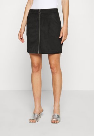 Mini-jupe en suede noire avec une fermeture éclair à l'avant, présentant une texture lisse et une forme ajustée, associée à des sandales à enfiler argentées.
