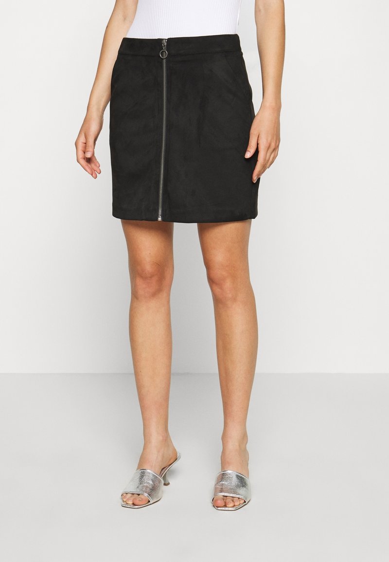 Mini gonna nera in suede con zip frontale, caratterizzata da una consistenza liscia e una forma aderente, abbinata a sandali argento slip-on.