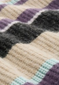 Couverture tricotée plus grande avec des rayures ondulées alternées en beige, gris foncé et violet, avec un accent teal clair le long des bords.
