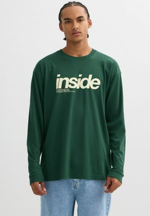 Camiseta de manga larga de color verde oscuro con un ajuste holgado, que presenta un gran gráfico de texto blanco "inside" y texto adicional abajo en una fuente más pequeña.