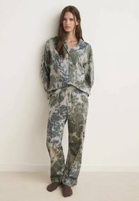 Conjunto de pijama de dos piezas hecho de tela texturizada en tonos verdes y beiges con un patrón similar al mármol; presenta una parte superior abotonada y pantalones elásticos.