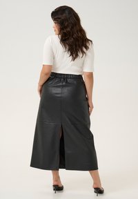 Fustă maxi din piele neagră, cu un brâu elastic și o deschidere pe spate. Asortată cu un top alb, ajustat, cu mânecă scurtă și tocuri negre.