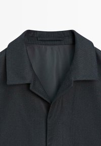 Czarny kołnierz odzieży, charakteryzujący się gładką fakturą i dopasowanym krojem. Materiał wydaje się lekko teksturowany z delikatnym połyskiem.