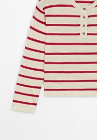 Beżowa koszula henley z długim rękawem, z poziomymi czerwonymi i czarnymi paskami oraz trzema brązowymi guzikami na listwie przy piersi.