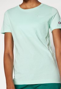 Jasnozielona, miękka bawełniana koszulka z krótkimi rękawami, okrągłym dekoltem i małym, haftowanym logo na piersi. Miękka w dotyku, dopasowany krój.