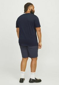 Tamsiai mėlyna trumpa rankovė t-shirt su apvalia iškirpte, derinama su atitinkančiomis tamsiai mėlynomis šortais. Vokas su baltais kojiniais ir juodais batais. Lygus audinys.