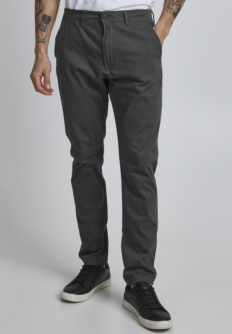Mørkegrå chinos laget av mykt stoff, med rett ben-design, frontlommer og knappestang. Brukt med svarte joggesko.