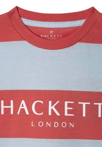 Červené a světle modré pruhované tričko s kulatým výstřihem; má na přední straně výrazné bílé logo "HACKETT LONDON".