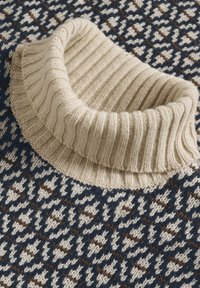 Chunky bežasti rebrasti ovratnik na tamnoplavoj, bijeloj i smešnoj pletenoj košulji.