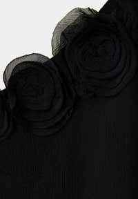 Tissu noir avec trois applications de fleurs en voile superposées disposées en rangée le long du bord.