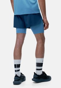 Completo sportivo da uomo con maglietta azzurra a maniche corte, pantaloni corti blu, pantaloni aderenti blu sotto, e scarpe da ginnastica nere con calzini bianchi a righe.