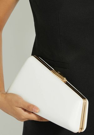 Witte rechthoekige clutch van glad materiaal, met een goudkleurige sluiting en accenten. In één hand vastgehouden tegen een donkere outfit.