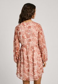 Blommönstrad klänning med långa ärmar, en gathered midja och en flödande silhuett i pastellrosa och röda nyanser med textilstruktur.