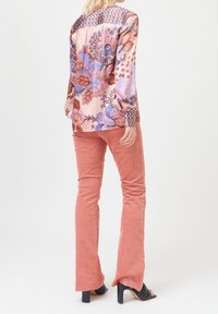 Blouse florale multicolore à manches longues, avec un pli dans le dos et un empiècement à motif. Associée à un pantalon flare en velours côtelé rose et des sandales à talons noires.