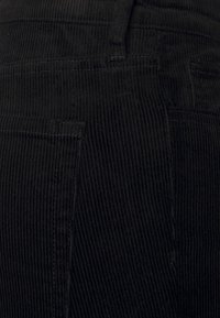 Svart kordfloret tyg med vertikal ribbad textur, som har fickdetaljer och en figurnära midja. Inga synliga metalldelar eller dekorationer.