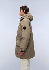 Beige parka jakke med hætte, med et rundt mærke på venstre ærme, justerbar snor og en frontlomme. Glat tekstur.